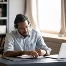 man writing notes from his laptop with headset on