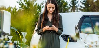 Woman looking at her mobile phone while the car is charging