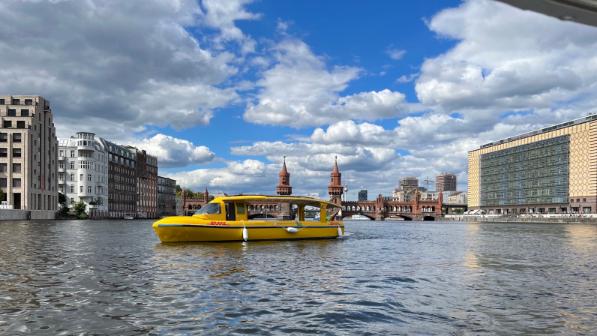 Das DHL-Solarschiff fährt auf der Spree in Friedrichshain-Kreuzberg. Im Hintergrund sieht man die Oberbaumbrücke.