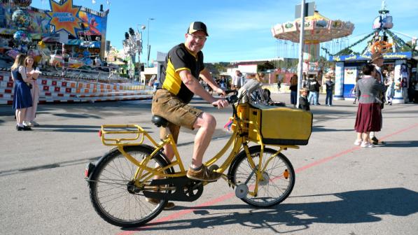 Wiesn-Zusteller Gerald Nadler unterwegs mit dem Dienstrad vor einem Fahrgeschäft.