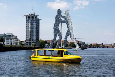 Das DHL-Solarschiff fährt auf der Spree am Molecule Men vorbei. 