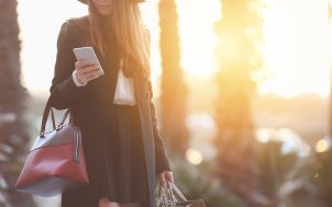 Woman carries shopping bags and looks at her cell phone