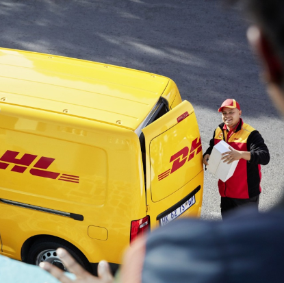 A DHL delivery person stands beside a yellow DHL van, holding a package. The photo, taken from an elevated perspective with a person in the foreground, highlights DHL's expertise in affordable small business shipping.