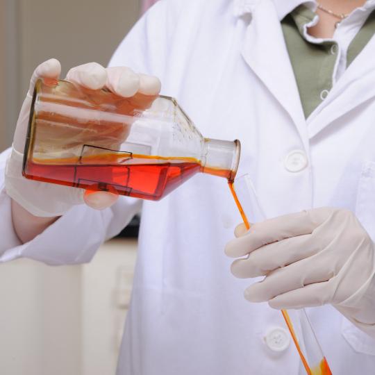 Scientist sampling red chemical from a glass bottle