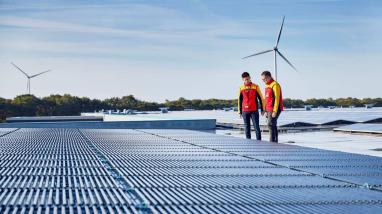 DHL employes at a solar energy farm with wind mills in the background 