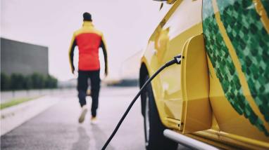 Electric vehicle charging with a DHL delivery driver in the background 