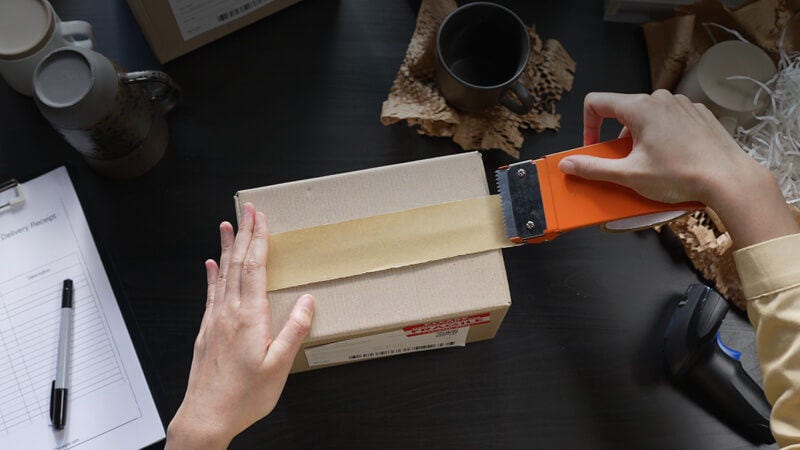 person adding packing tape to the top of a gift box