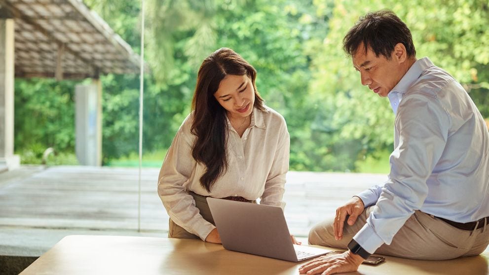 A male and female employee have a discussion at a table with a laptop between them