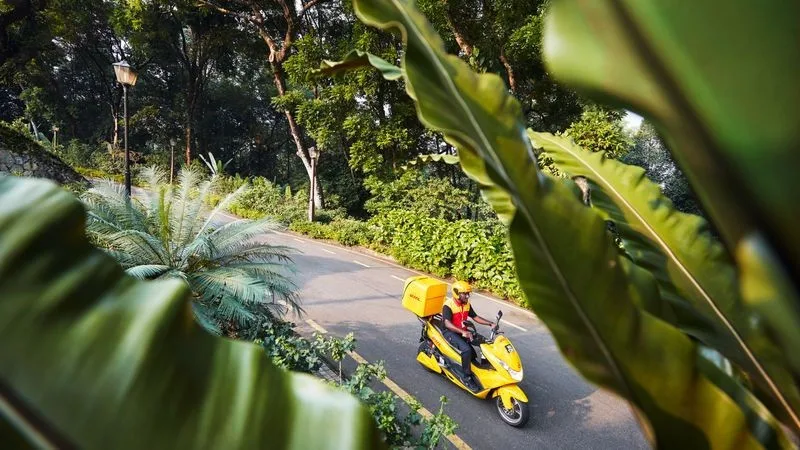 DHL parcel carrier driving through nature with scooter.