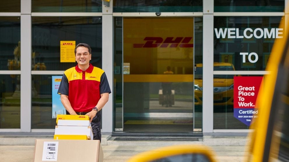 A male DHL employee transports parcels on a handcart in front of a DHL ServicePoint.