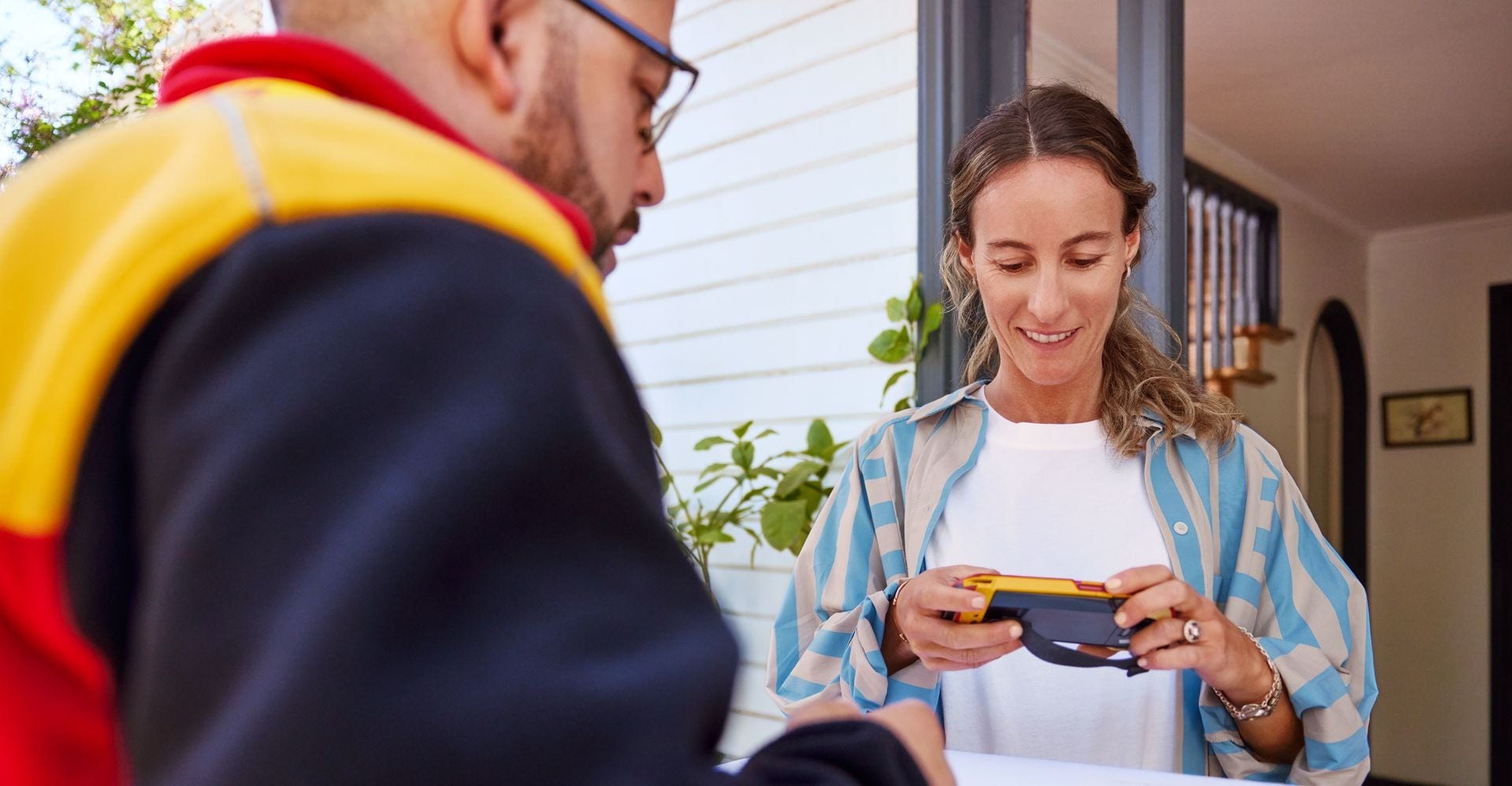 A dhl express new zealand employee hands a white parcel to a female customer while she signs a scanner.