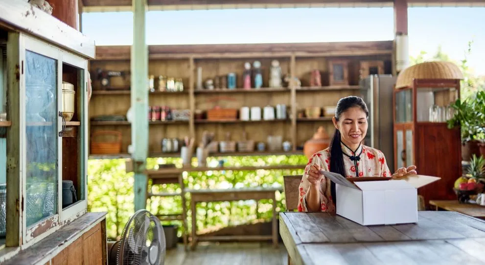 Asian woman smiling while opening a package on a table