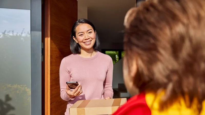 woman holding a mobile phone and parcel while discussing courier pickup service with a dhl employee