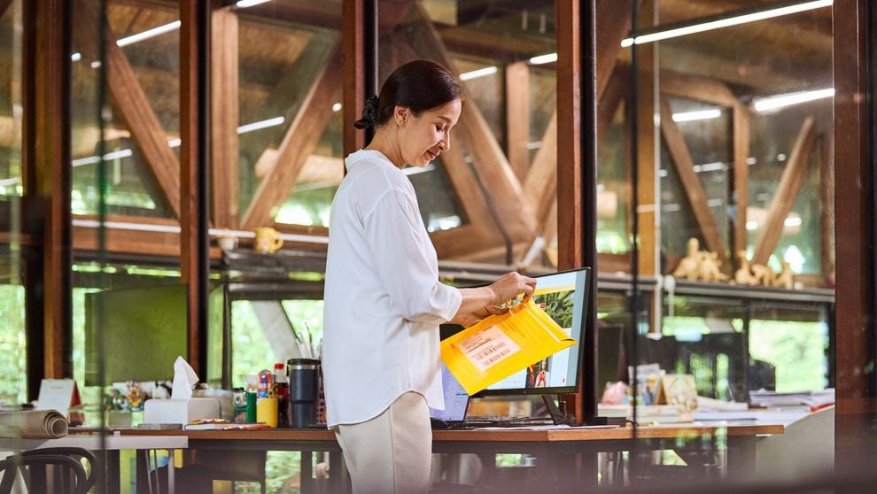 A woman opens an express envelope while standing in front of a desk.