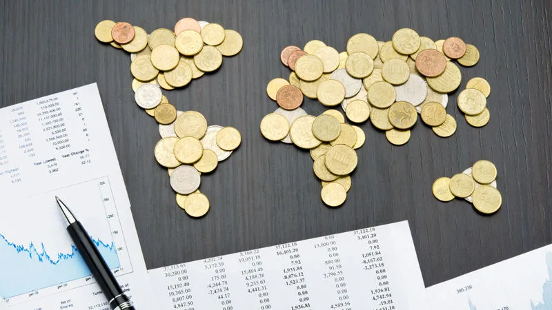 Office desk with world map made of money coins and report sheets