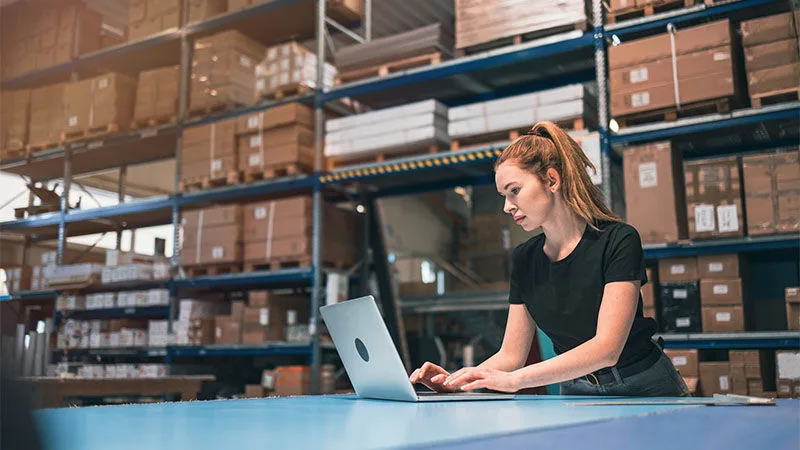 woman typing on a laptop in a warehouse