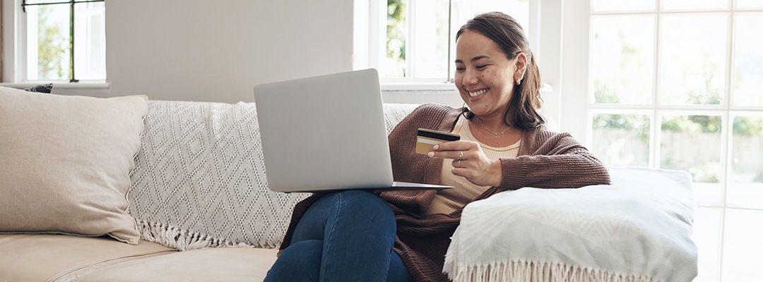 woman holding a credit card smiling at a laptop screen