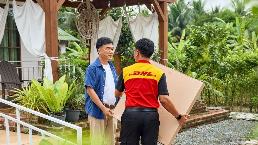 A DHL Express deliveryman hands a parcel to a customer on the terrace of his house.