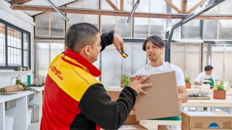 a dhl employee scanning the parcels for pick up as the male start-up employee looks on