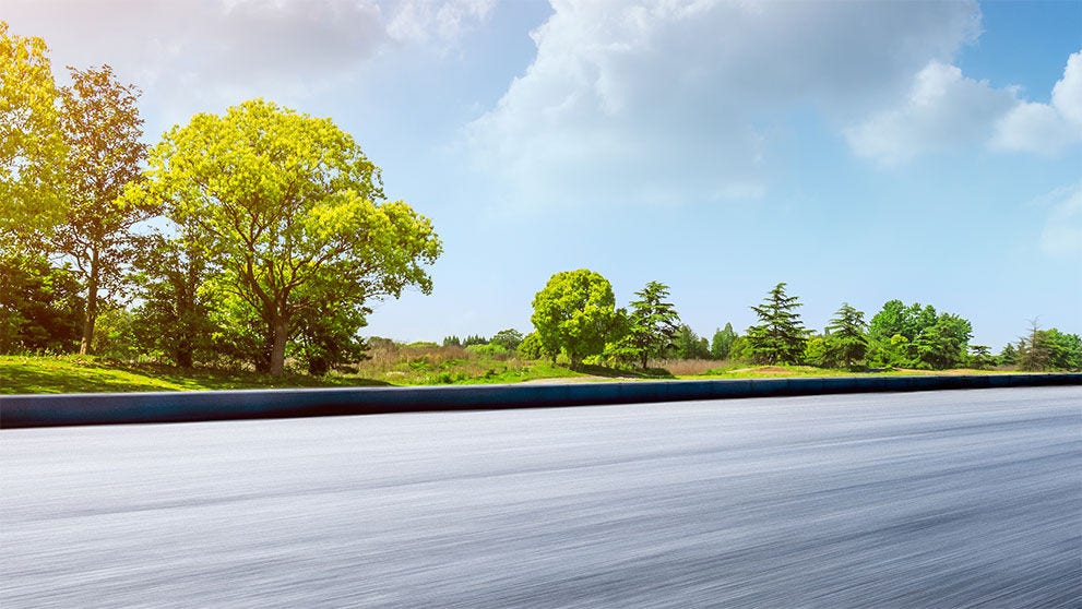 Fast moving asphalt road and green forest landscape.