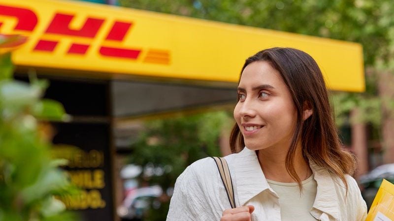 A customer with an express envelope walking in front of a DHL service point.