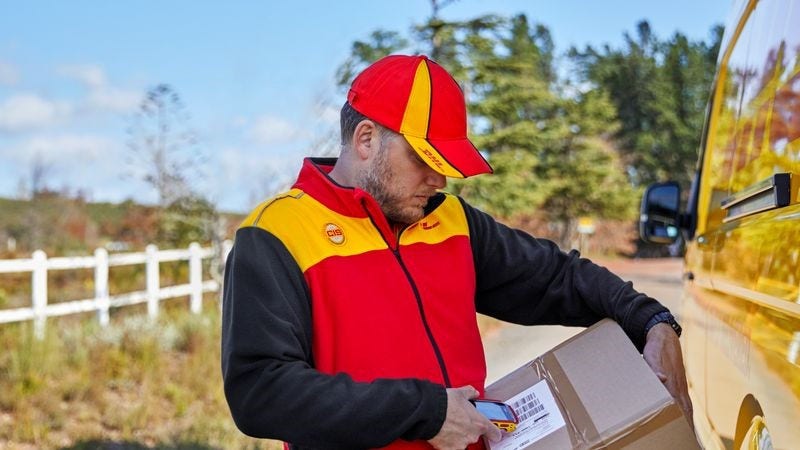 Postman scans parcel next to delivery can in the countryside