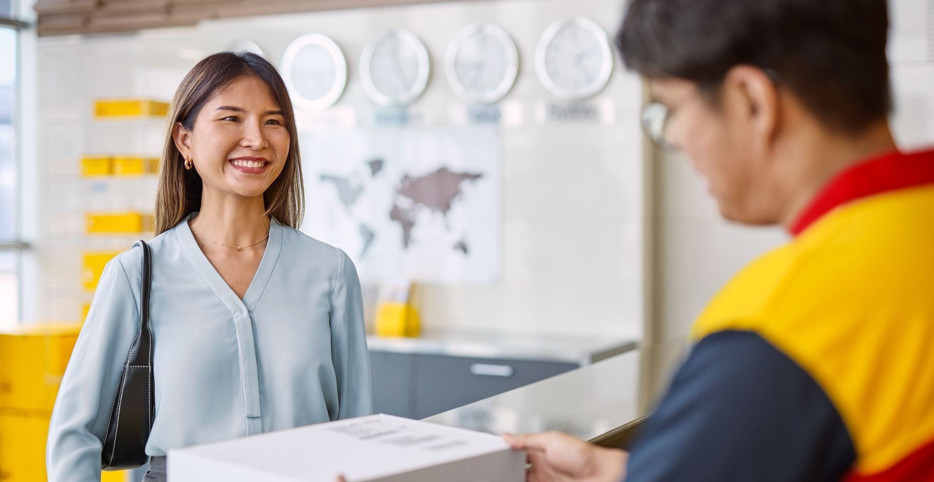 A male DHL employee hands a parcel to a female customer.