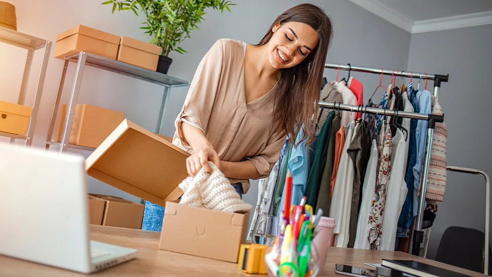 Young woman selling products online and packaging goods for shipping. Women, owener of small business packing product in boxes, preparing it for delivery