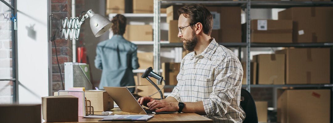 man in a warehouse typing on a laptop