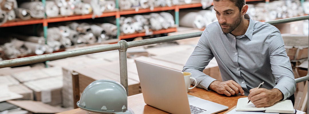 man writing in notebook and looking at laptop screen