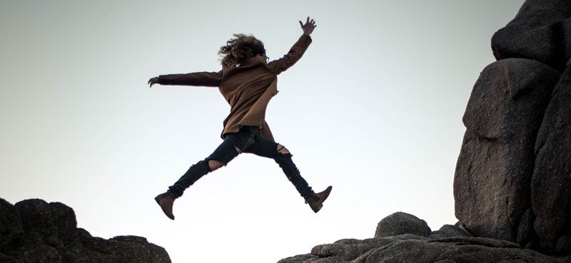 Woman leaping across gap in stoney mountain