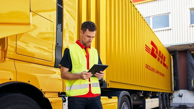 a dhl employee focusing on a tablet while standing in front of a delivery truck