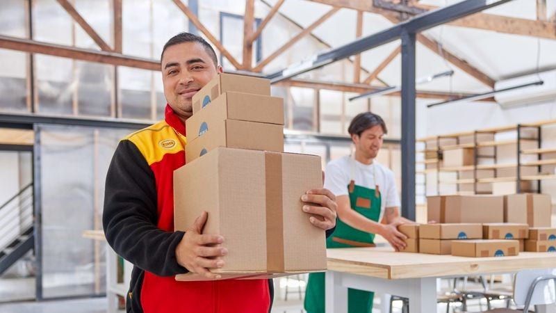 A DHL employee in uniform delivers packages to a customer at a small business.