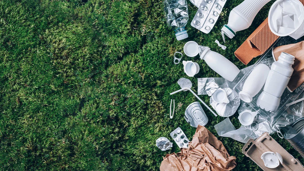 Food plastic packaging, trash on green moss background after picnic in forest.