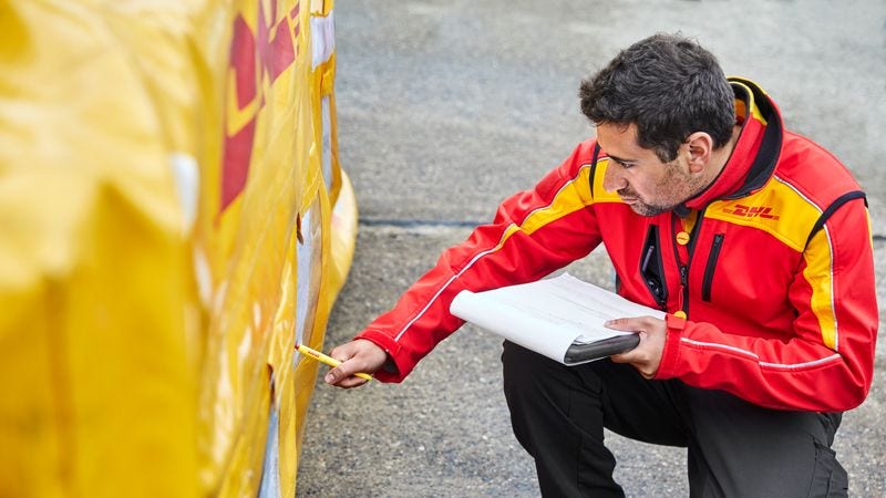 A DHL employee reads export documents in front of freight boxes.