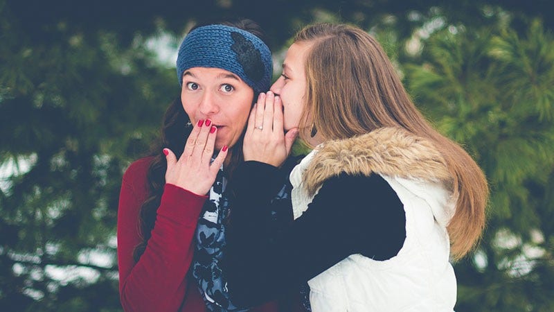 one woman whispering in another woman's ear