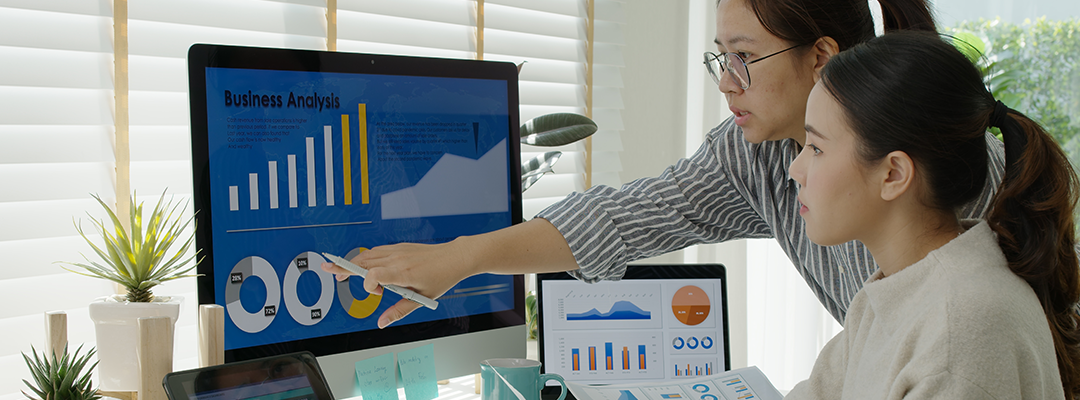 woman showing another lady stats on a computer screen