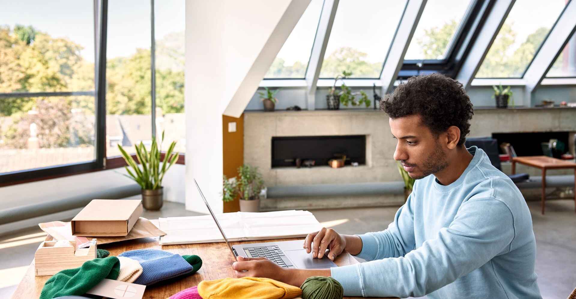 Man with a beanie business working on his laptop at home, with city view.