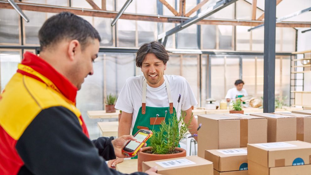 A male DHL employee is handling his scanner for picking up parcels from an SME business owner