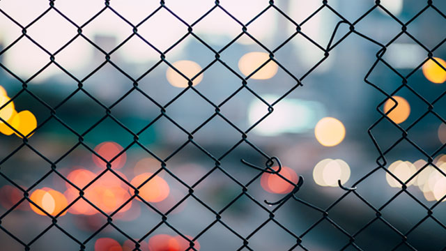 Hole in a metal fence with blurred lights