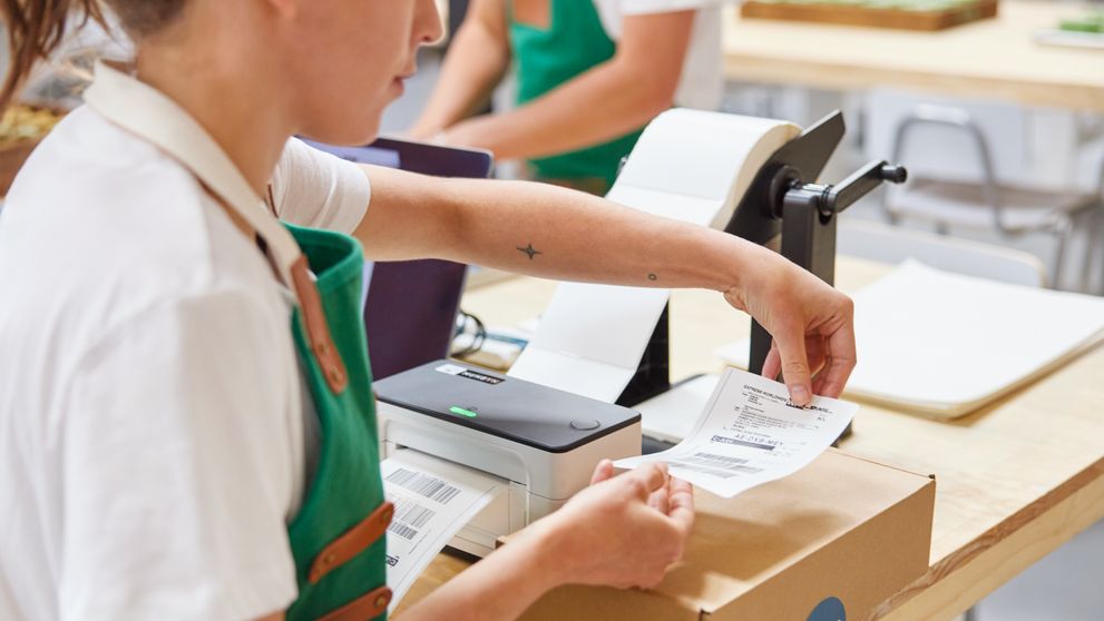 a woman is sticking a bill on a parcel to prepare it for shipping.