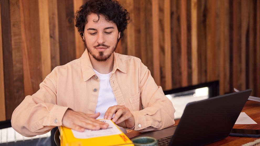 A male livestream salesperson is sticking a label on a DHL express parcel at home.