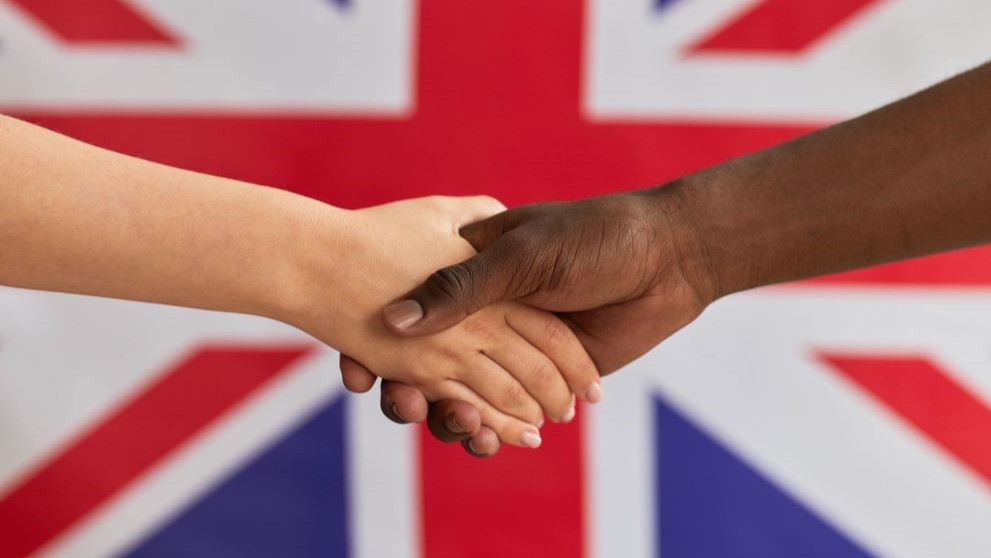 Two people shaking hands behind UK flag