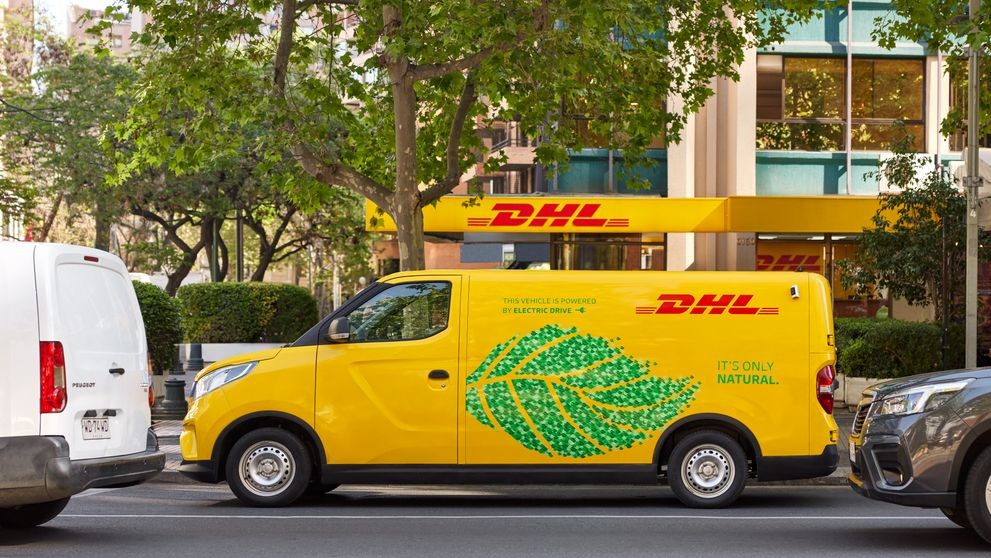 An electric DHL van is standing outside a DHL service point.