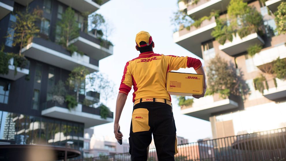 ack view of a male DHL employee holding a DHL box and looking up at a building